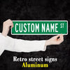 A hand holds up a green aluminum street sign with the text CUSTOM NAME ST