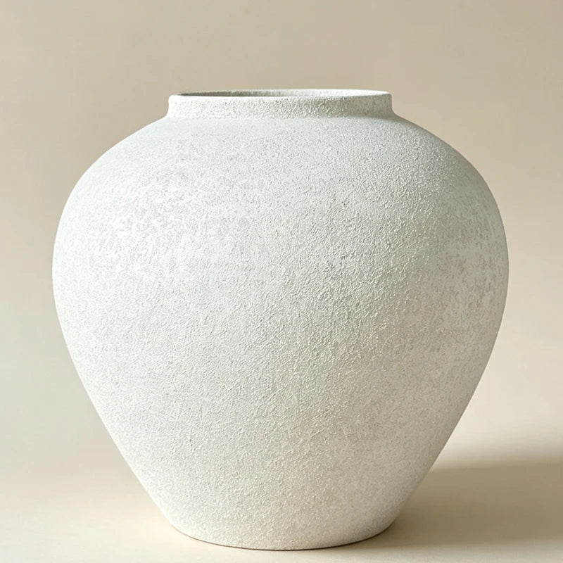 A round, light gray ceramic vase with a textured finish, photographed from a slight angle.