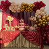 A balloon garland arch display featuring burgundy, gold, and white balloons on a draped table.