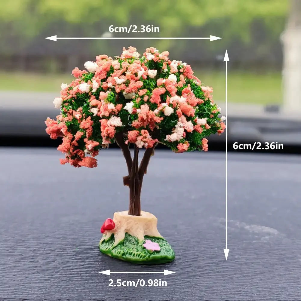 A miniature tree ornament featuring pink and white flowers on a small base, displayed on a dark surface.