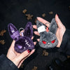 A hand holds a dark purple velvet bunny plush keychain with silver rings against a dark background.
