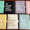 A collection of colorful 100 envelope savings challenge binders and organizers displayed on a wooden surface.