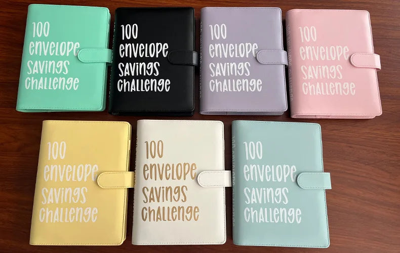 A collection of colorful 100 envelope savings challenge binders and organizers displayed on a wooden surface.