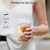 A person holds a clear plastic cup filled with iced coffee, demonstrating no leak or spill.