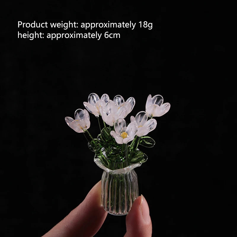 A small bouquet of white glass flowers in a clear glass vase being held by a hand.