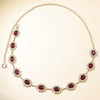 A delicate gold chain necklace featuring round red gemstones and clear accent stones.