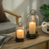 Two antique brass metal candle holders with glass domes and lit candles resting on a wooden table.
