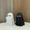 A white ghost figurine and a black ghost figurine displayed against a wooden background.
