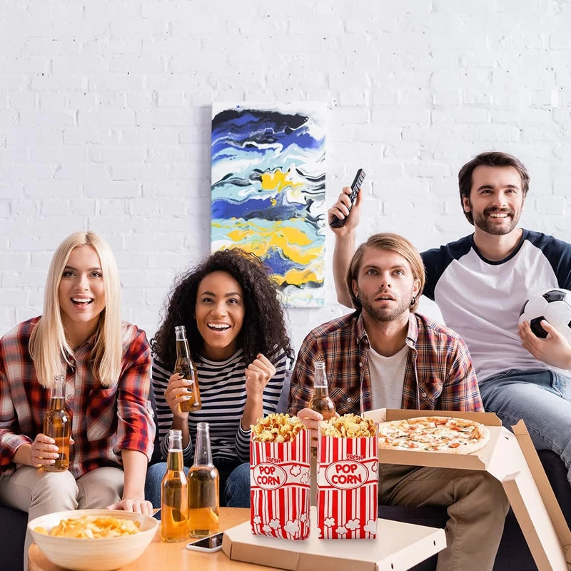 Three people smiling while holding popcorn buckets in front of a white brick wall.