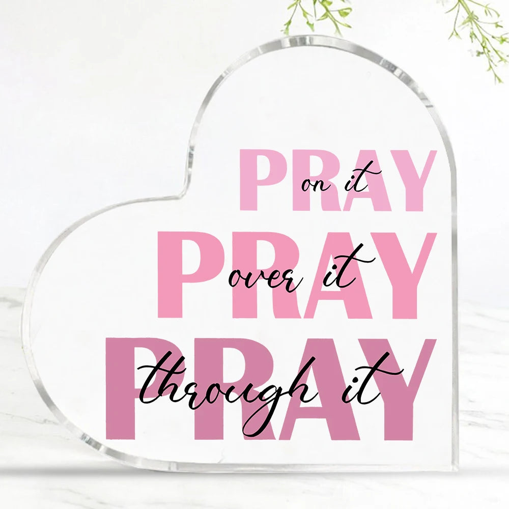 A clear acrylic heart-shaped sign with pink text that reads Pray on it Pray over it and Pray through it