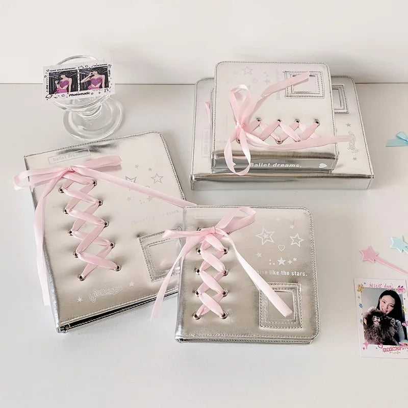 Silver leather photo albums with pink ribbons and star accents displayed on a white surface.