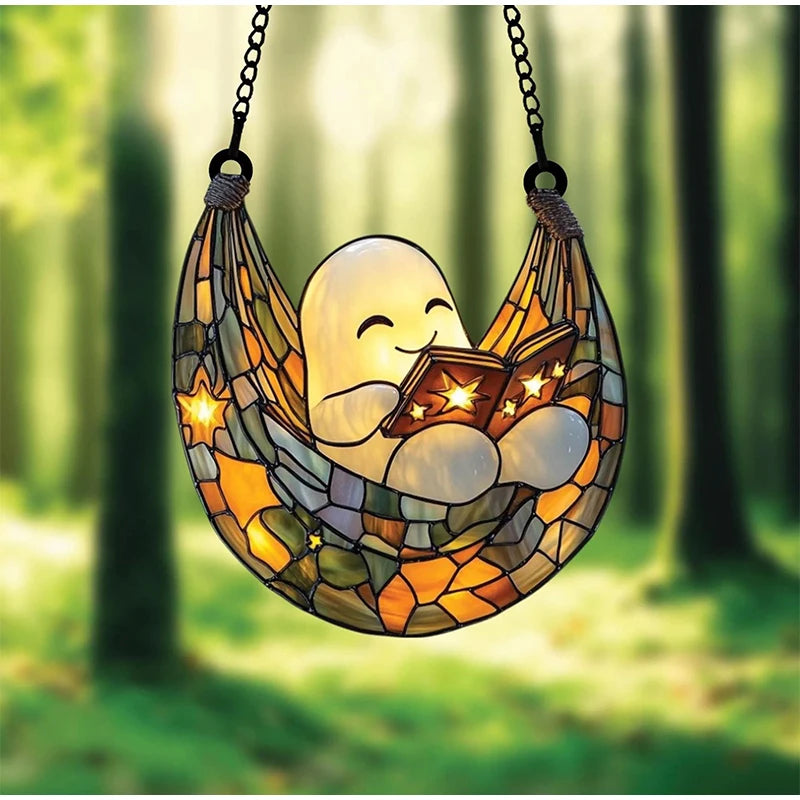 A glass hanging decoration shaped like a smiling ghost reading an open book, suspended by chains.