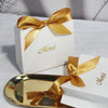 A gold-edged paperboard thank you gift bag tied with a satin ribbon, resting on a white surface.