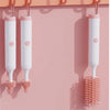 A set of white electric baby bottle cleaning brushes hanging on a pink wall.