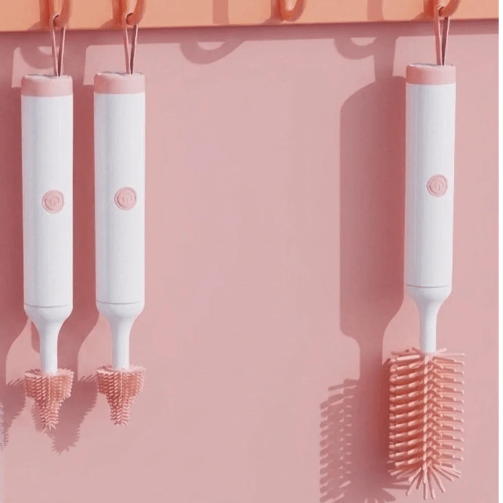 A set of white electric baby bottle cleaning brushes hanging on a pink wall.