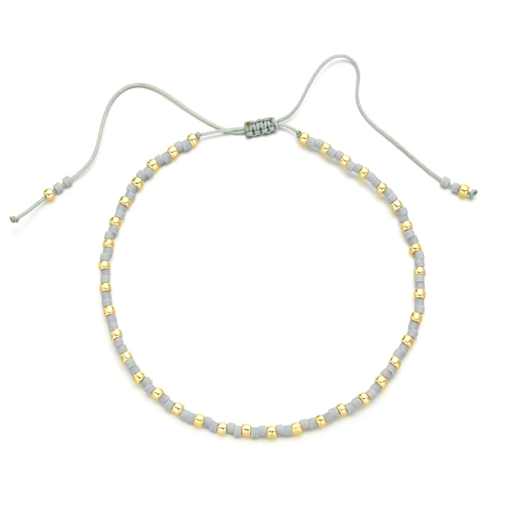 Handmade boho glass bead bracelet with adjustable cord featuring small gold and gray beads.