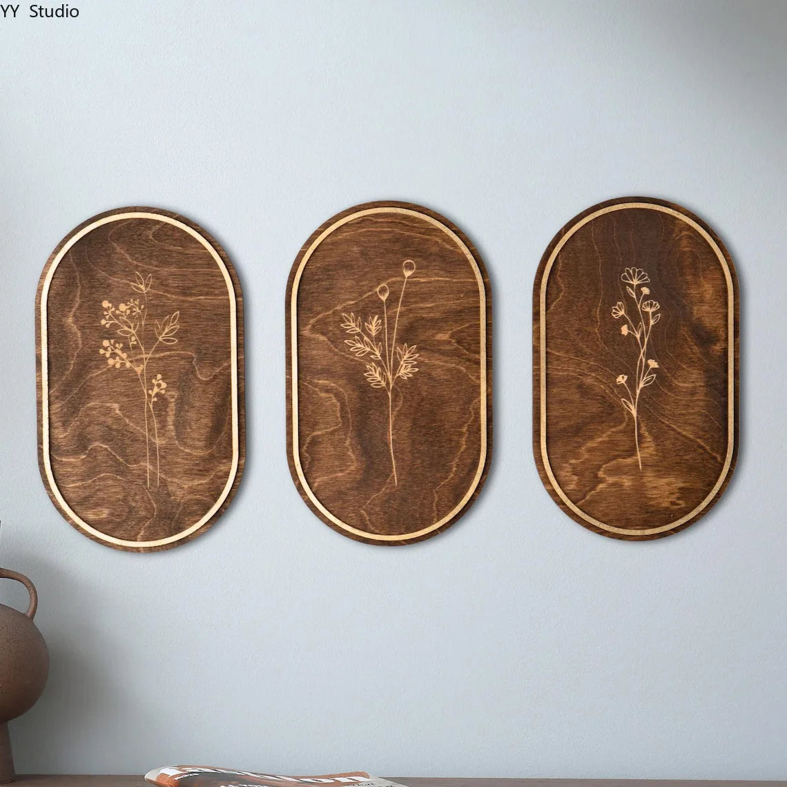Three oval wooden wall decor pieces featuring delicate dried floral silhouettes on a neutral background