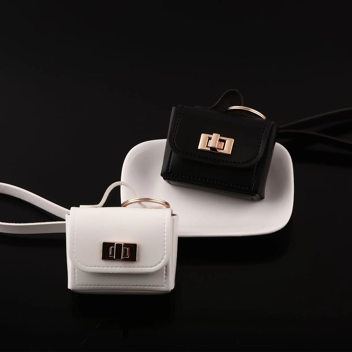 A pair of mini black and white leather openable bags with gold hardware resting on a black surface.