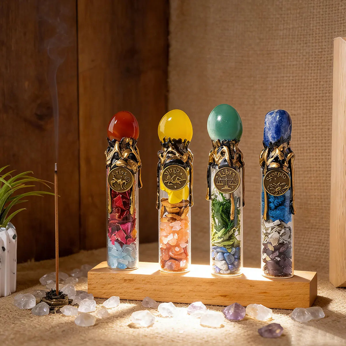 Four glass bottles filled with natural healing stones and zodiac symbols displayed on a wooden surface.
