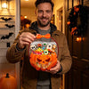 A man holds an orange carved pumpkin Halloween treat bag filled with candy and treats.