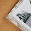 A rustic wooden photo frame with distressed white and brown paint, displaying a blurred outdoor scene.
