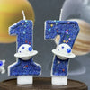 Two birthday candles shaped like the number 1 decorated with blue glitter and white planets against a blurred space backgroun