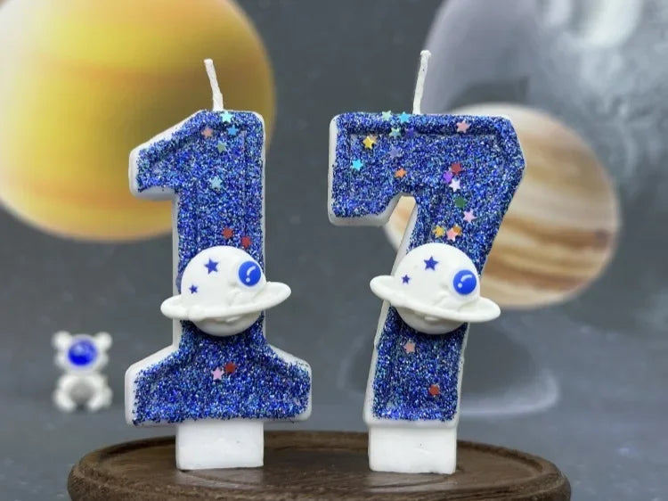 Two birthday candles shaped like the number 1 decorated with blue glitter and white planets against a blurred space backgroun