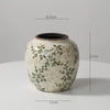 A cream-colored ceramic milk pitcher with a rustic glaze and pastoral green floral design.