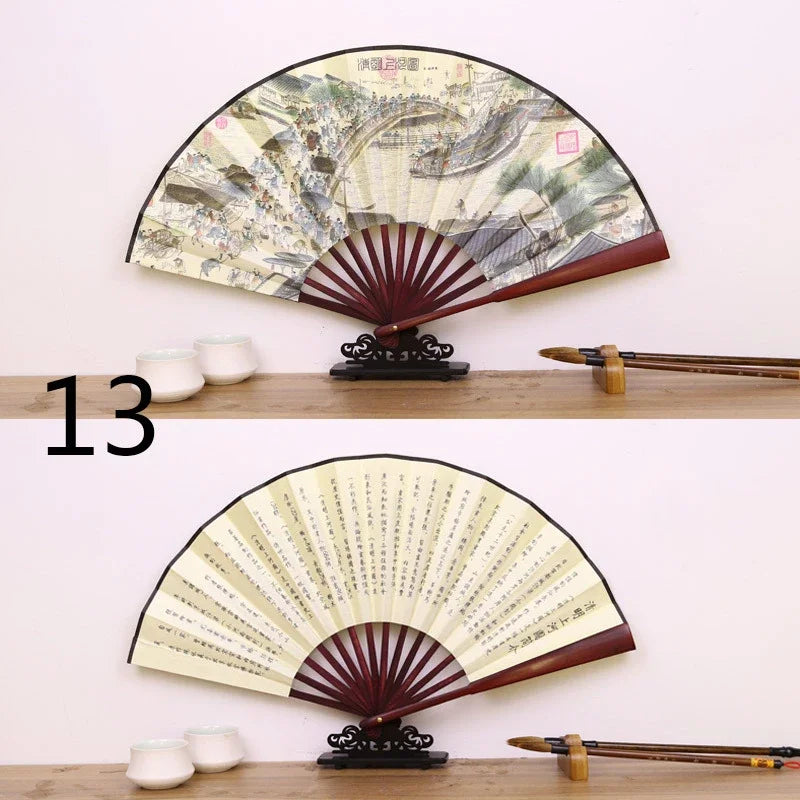 A vintage folding fan with a dark brown silk and bamboo frame and cream-colored paper, displayed on a wooden surface.