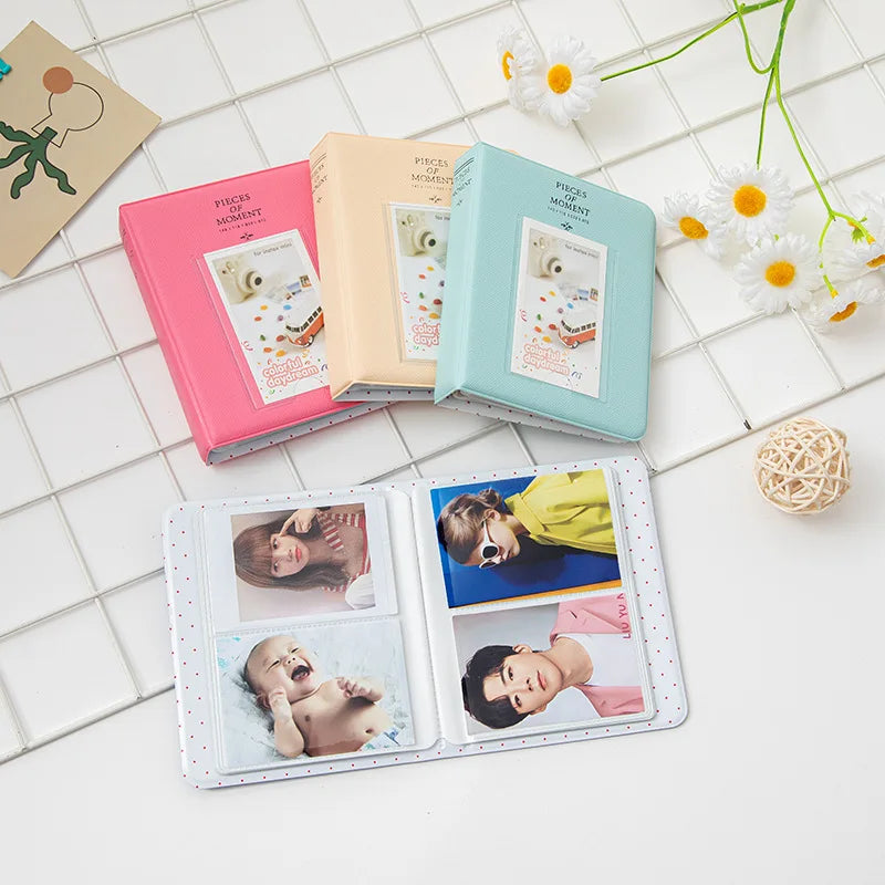 A collection of pink, beige, and teal compact photo albums for instant film displayed on a white surface.