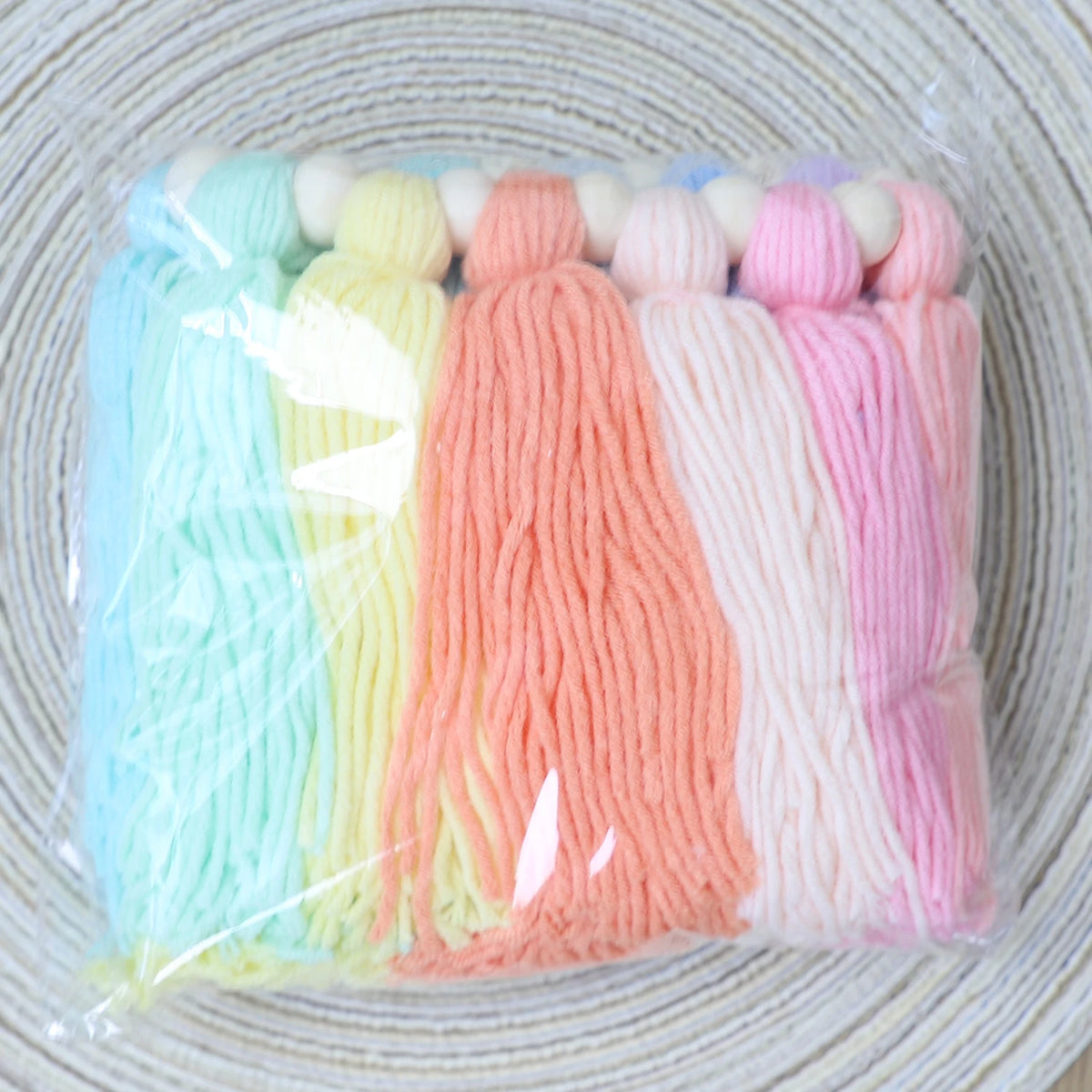 A bundle of colorful yarn strands in pastel shades, including blue, yellow, orange, pink, and white, tied together with woode