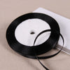 A black satin ribbon spool with a white core is shown on a light background.