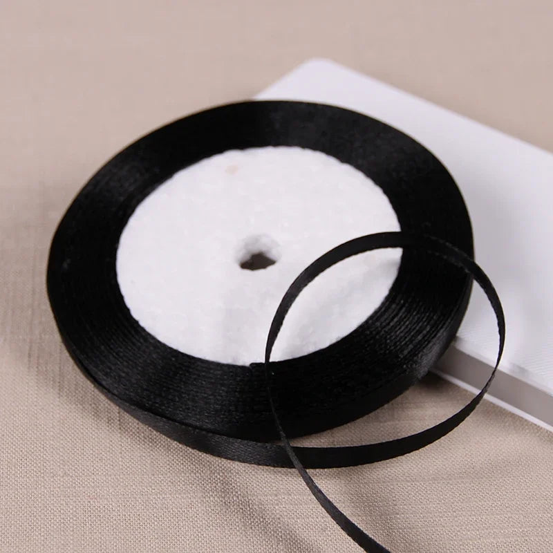 A black satin ribbon spool with a white core is shown on a light background.