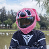 A person wearing a pink cartoon plush helmet cover for a full-face motorcycle helmet, outdoors near water.