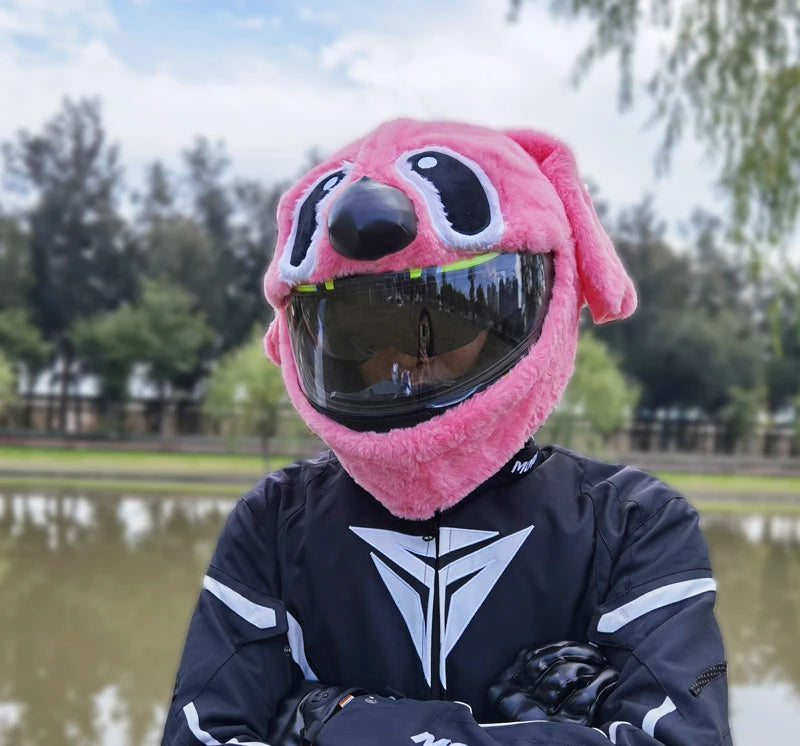 A person wearing a pink cartoon plush helmet cover for a full-face motorcycle helmet, outdoors near water.