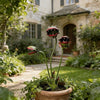 A decorative metal carnivorous flower garden stake with three flower heads growing in a potted plant surrounded by greenery.