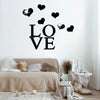 Black acrylic heart wall stickers spelling LOVE with a mirror finish on a white wall above a beige sofa.