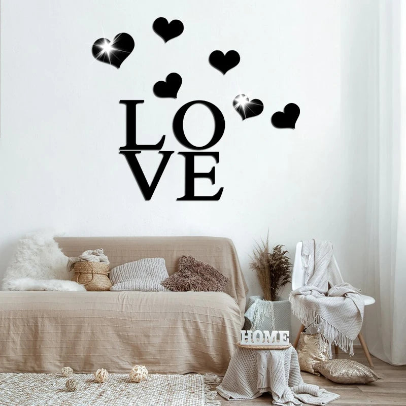 Black acrylic heart wall stickers spelling LOVE with a mirror finish on a white wall above a beige sofa.