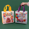 A hand is holding a reusable happy birthday gift bag with colorful balloons and a cake design.