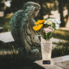 A stone angel sculpture holding a bouquet of yellow and white flowers in a solar grave memorial vase.