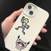 A light beige smartphone displaying a skull and a raccoon decal on the back, held by a hand.