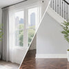 A tall artificial bamboo tree in a white pot displayed on a wooden staircase next to a window.
