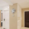 A modern circular wall clock with Arabic numerals is mounted on a beige wall in a hallway.