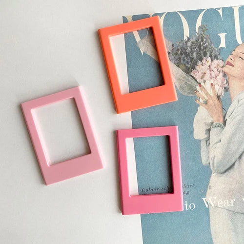 Three magnetic photo frames in orange, pink, and magenta against a blue background.