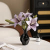 A black ceramic vase holds purple and green orchid flowers on a white table.