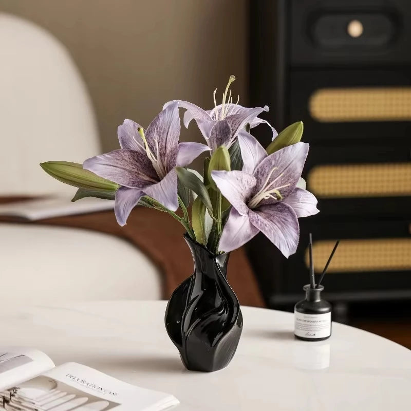 A black ceramic vase holds purple and green orchid flowers on a white table.