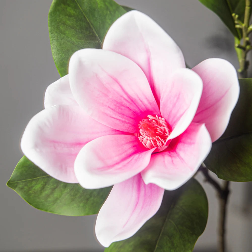 A close-up of a pink and white artificial magnolia flower with green leaves.
