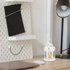 A white vintage hanging metal lantern with a yellow candle sits on a wooden desk.