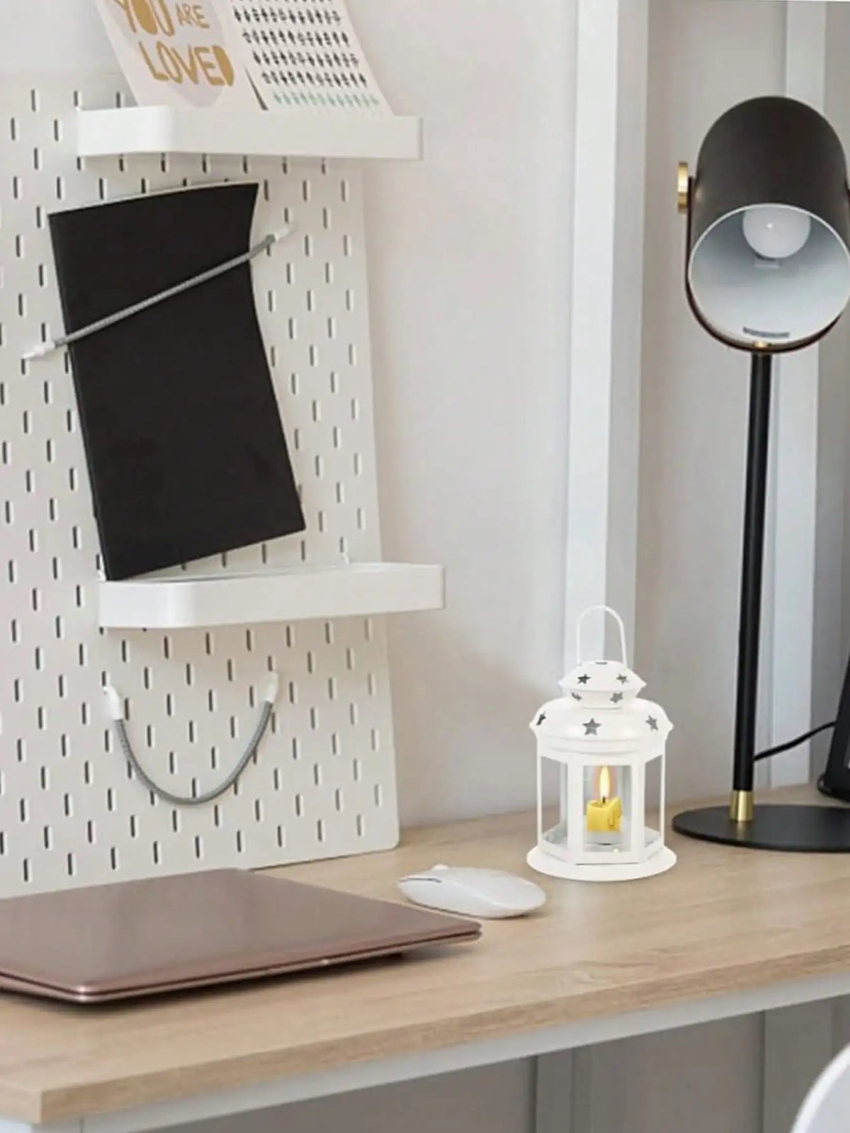 A white vintage hanging metal lantern with a yellow candle sits on a wooden desk.