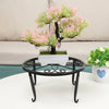 A decorative black metal plant stand with a saucer holding a small pink and green bonsai-style tree.